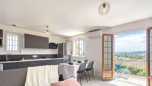 A modern kitchen with dark cabinets, a dining area with a table and chairs, and a balcony with a view of the countryside. - Fleurie by Interhome (Fréjus)