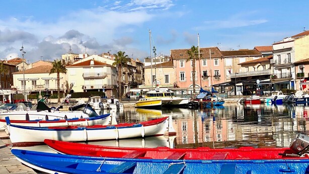 Un port de plaisance où sont amarrés des bateaux aux couleurs vives, entouré d’immeubles dotés de balcons, sous un ciel dégagé.