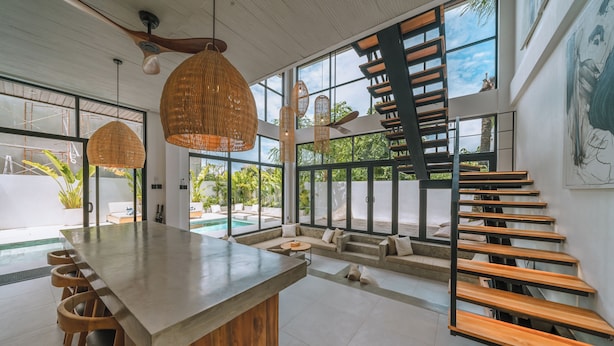 A spacious indoor area with a long wooden bench, a central island with stools, and a staircase with wooden steps.