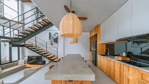 A modern kitchen with a central island, wooden cabinets, and a staircase with a glass railing.