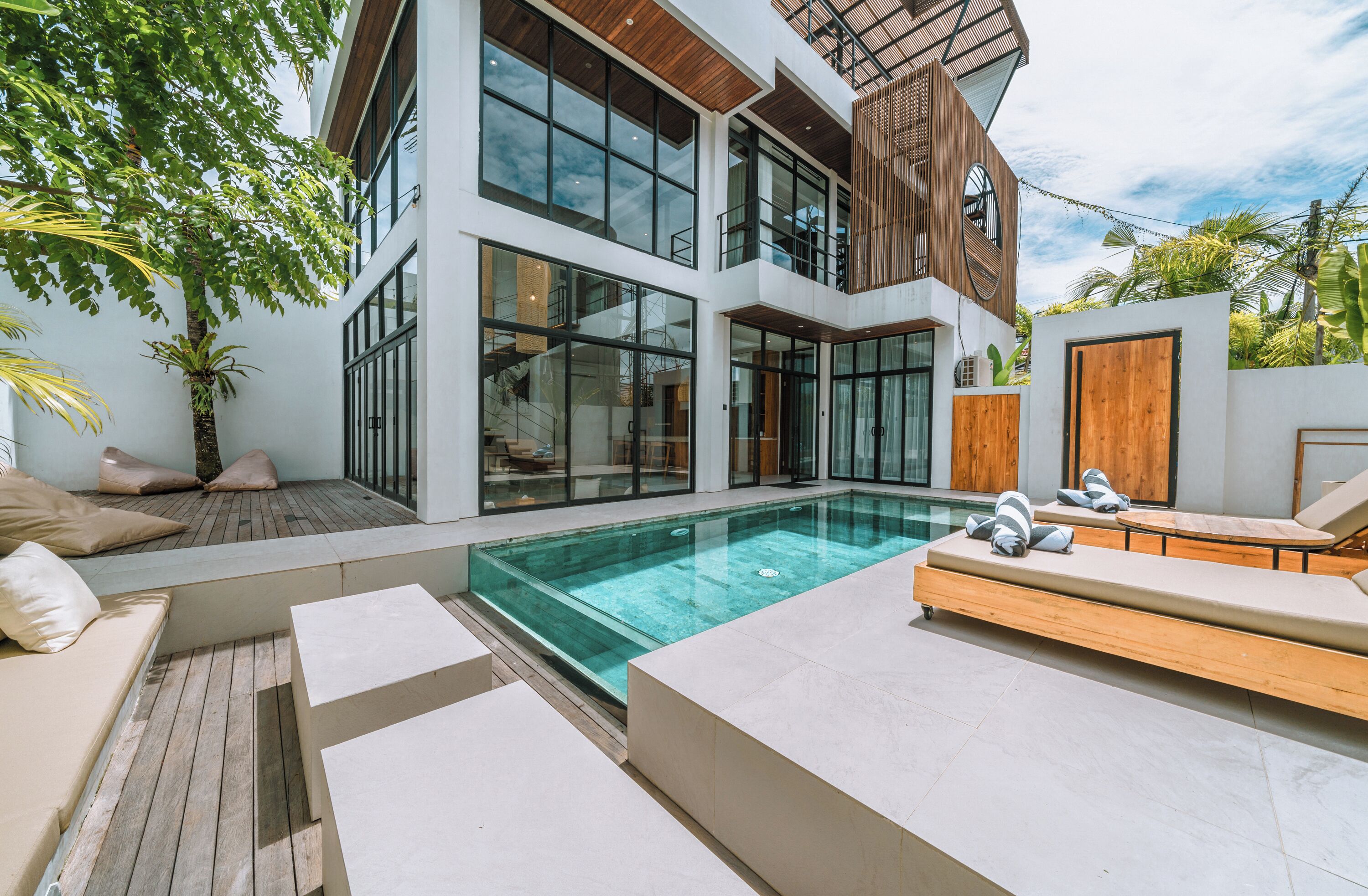 Une maison moderne dotée d’une grande baie vitrée, d’une piscine et d’un espace salon extérieur.
