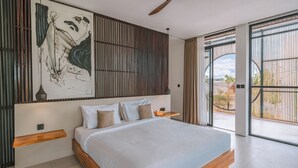 A modern bedroom with a large bed, a ceiling fan, a wooden headboard, and a large window with a view of the outdoors.