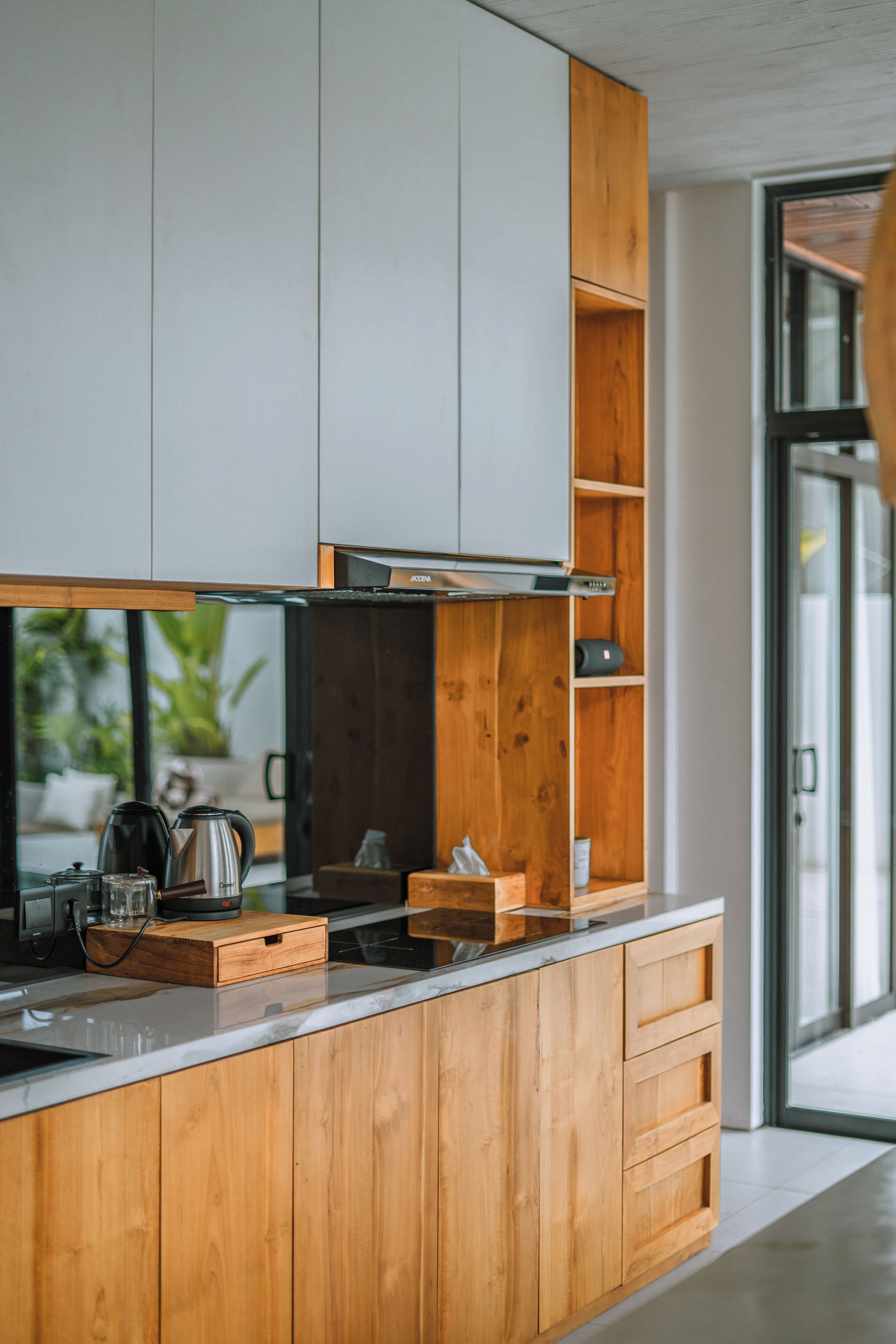 Een moderne keuken met houten kastjes, een roestvrijstalen afzuigkap en een glazen deur naar een lichte kamer.