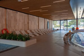 A spacious indoor area with a long row of lounge chairs, a small pool, and a modern ceiling design.
