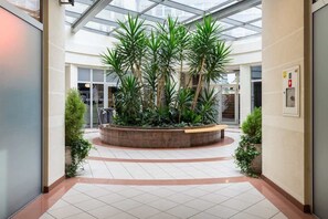 A spacious atrium with a central planter containing tall green plants, surrounded by a tiled floor and glass ceiling.