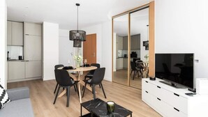 A modern living room with a dining area, a TV, and a kitchen in the background.