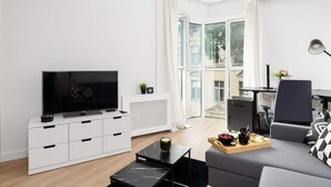 A modern living room with a flat-screen TV, a sofa, a coffee table, and a dining area with a tray of food.