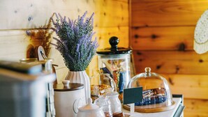 A kitchen counter with a coffee maker, a vase with lavender, a jar of preserves, and a glass dome covering a chocolate display.