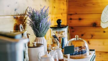 A kitchen counter with a coffee maker, a vase with lavender, a jar of preserves, and a glass dome covering a chocolate display.