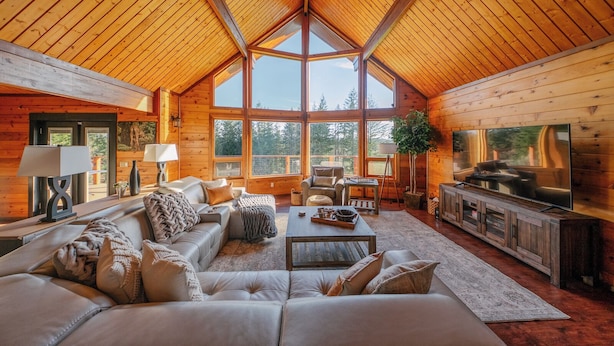 A spacious living room with a high ceiling, large windows, a fireplace, and a television.