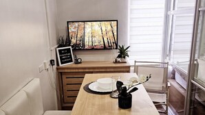 Un área de comedor con una mesa de madera dispuesta para dos personas, un televisor arriba y un amplio ventanal corredizo a la derecha.