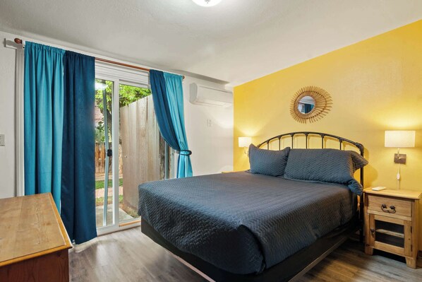 Een slaapkamer met een bed, een nachtkastje, een lamp en uitzicht op de omgeving door een schuifdeur.