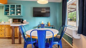 A kitchen with a dining area, a TV mounted on the wall, and a window with curtains. - Shared Backyard Oasis • Hot Tub + Grill (Moab)
