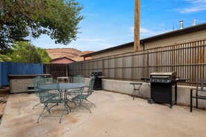 Een terras buiten met een tafel, stoelen, een grill en een barbecue.