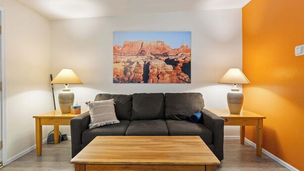 A living room with a sofa, coffee table, and two lamps. A large painting of a canyon is on the wall. - Shared Backyard Oasis • Hot Tub + Grill (Moab)