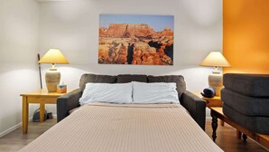 A bedroom with a bed, two bedside tables with lamps, a chair, and a large landscape painting on the wall. - Shared Backyard Oasis • Hot Tub + Grill (Moab)