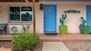 Un bâtiment avec une porte bleue, une enseigne portant le chiffre « 2 » et une autre indiquant « Rose Tree Lane ». On y trouve deux jardinières vertes contenant des cactus.