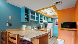 Une cuisine aux murs de couleur turquoise, avec un îlot central en bois et un four à micro-ondes placé à droite.
