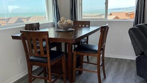 Un comedor con una mesa y sillas de madera, un ventilador de techo y ventanas grandes con cortinas.