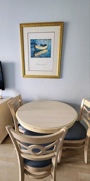 A round wooden table with four chairs, a framed picture on the wall, and a television on a stand. - Oceanview Efficiency DW409 (Myrtle Beach)