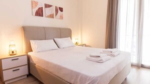 A neatly made bed with white linens and two pillows, a bedside table with a lamp, and artwork on the wall. - Trendy 2 Bd Apt in Galatsi (Athens)