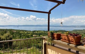 A balcony with terracotta planters, a hanging light bulb, and a view of a lake and distant mountains. - 1 bedroom gorgeous apartment in Montefiascone (Montefiascone)