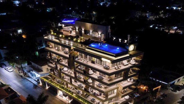 A multi-story hotel with a rooftop pool, multiple balconies, and well-lit outdoor areas.