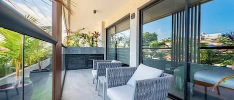 Un balcon avec des fauteuils en osier et une porte vitrée donnant sur une terrasse.
