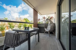 A balcony with a table and chairs, a wicker chair, and a view of the cityscape.