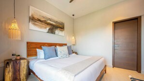 Un dormitorio con cabecera de madera, una cama grande con ropa blanca, varios almohadones, un cuadro abstracto colgado en la pared y una puerta de madera.
