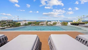 A rooftop pool with lounge chairs, a clear view of the ocean, and a cityscape in the background. - Kippal Holbox 2 Bedroom 2 Baths and a Private Balcony (San Miguel de Cozumel)