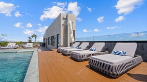 Zona de piscina en la azotea con sillones de descanso y un edificio moderno al fondo.