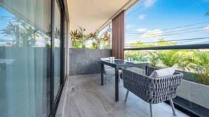 A balcony with a table and chairs, a view of greenery, and a clear sky. - Kippal Holbox 2 Bedroom 2 Baths and a Private Balcony (San Miguel de Cozumel)