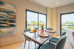 Un comedor con una mesa lista para dos personas, un florero con flores amarillas y un cuadro en la pared.