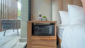 Un dormitorio con una cama, una mesita de noche con un dispositivo electrónico negro, una silla y una ventana con persianas.