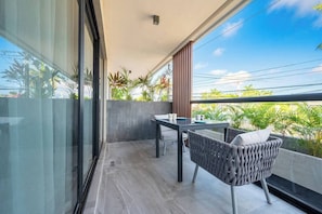 Un balcon avec une table et des chaises, une paroi en verre et une vue sur la verdure.