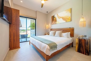 Une chambre moderne avec un grand lit, une télévision, un ventilateur de plafond et une vue sur l’extérieur.