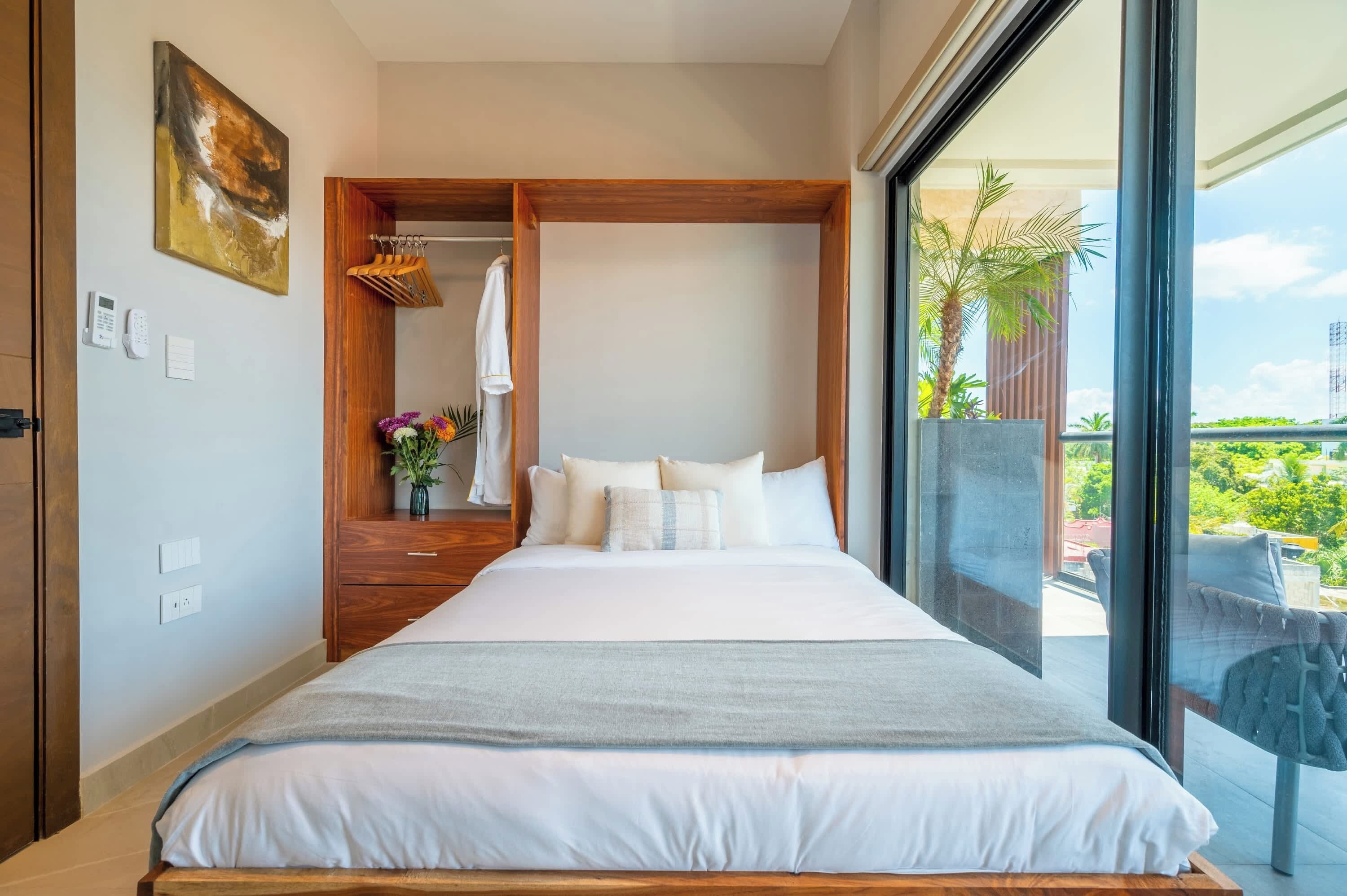 A hotel room with a large bed, a wooden wardrobe, a bathroom with a towel rack, and a balcony with a view.