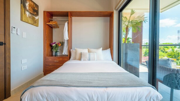 A hotel room with a large bed, a wooden wardrobe, a bathroom with a towel rack, and a balcony with a view.