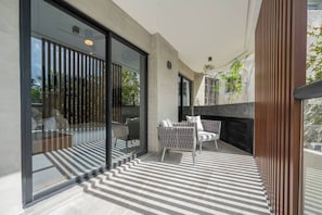A modern balcony with a glass door, a patterned floor, and a seating area with two chairs.