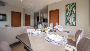 A dining area with a table set for four, a kitchen in the background, and a painting on the wall. - Kippal Apartamento con vista al mar (San Miguel de Cozumel)