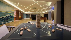 En rummelig lobby med et moderne design, der indeholder et stort bord med træklodser og et Jenga-tårn, et billardbord og et muralmaleri på væggen.