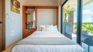 A hotel room with a large bed, a wooden wardrobe, a hanging towel rack, and a view of the outdoors. - Kippal Tulum  2 Bedroom 2 Baths  Ocean View Balcony (San Miguel de Cozumel)