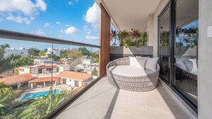 A balcony with a round seating area, a glass door, and a view of a swimming pool and buildings.