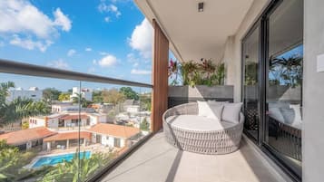 Een balkon met een rond zitgedeelte, een glazen deur en uitzicht op een zwembad en gebouwen.