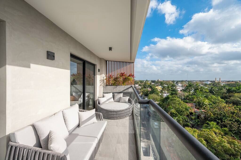 En balkon med en sofa og et rundt siddeområde, med udsigt over en by og grønne områder.