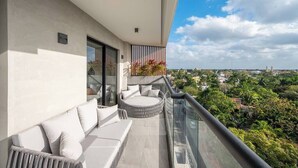 Ein Balkon mit einer Couch und einer runden Sitzecke, mit Blick auf eine Stadtlandschaft mit Grünflächen.