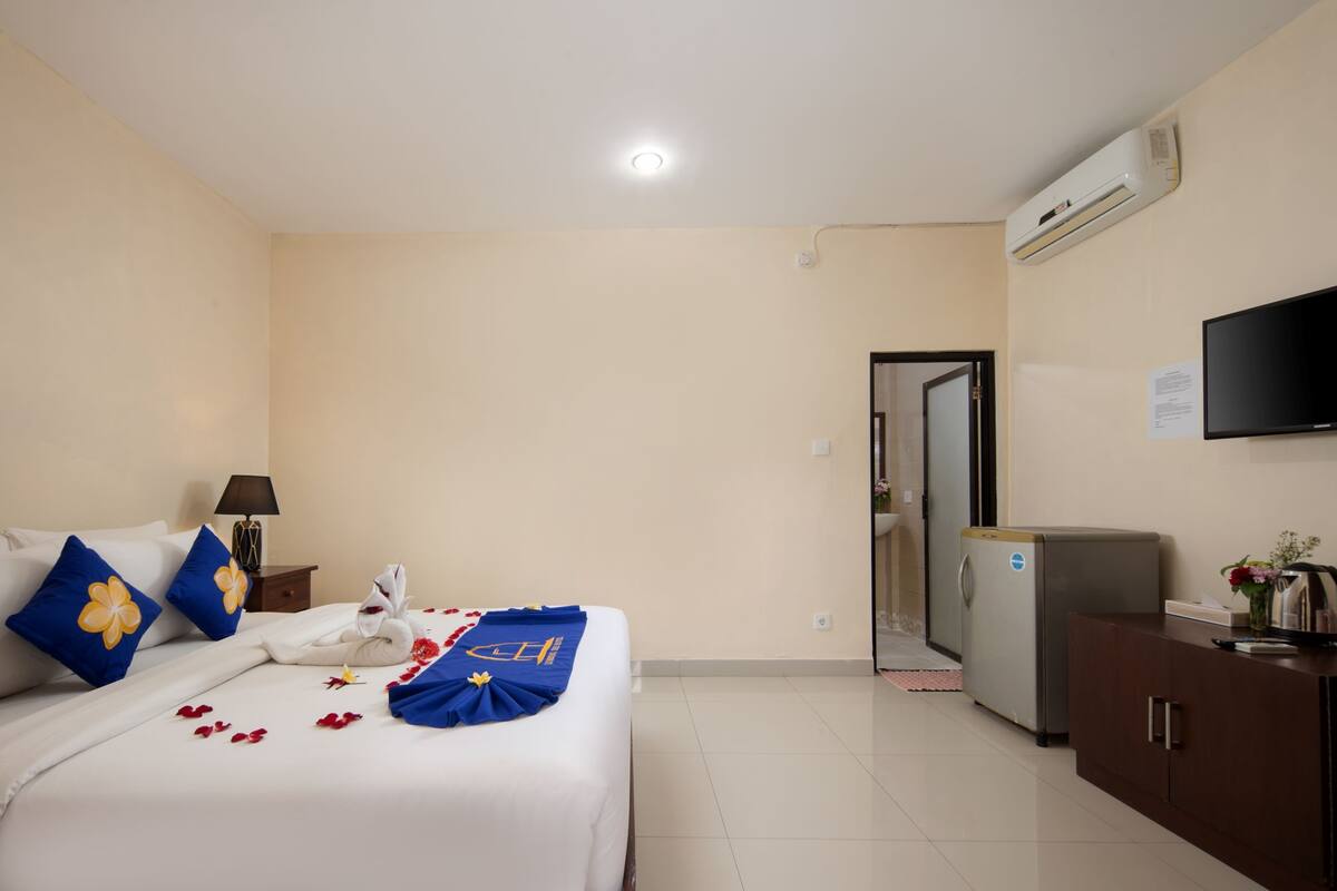 A hotel room with a bed, a television, a refrigerator, and a door leading to another room.