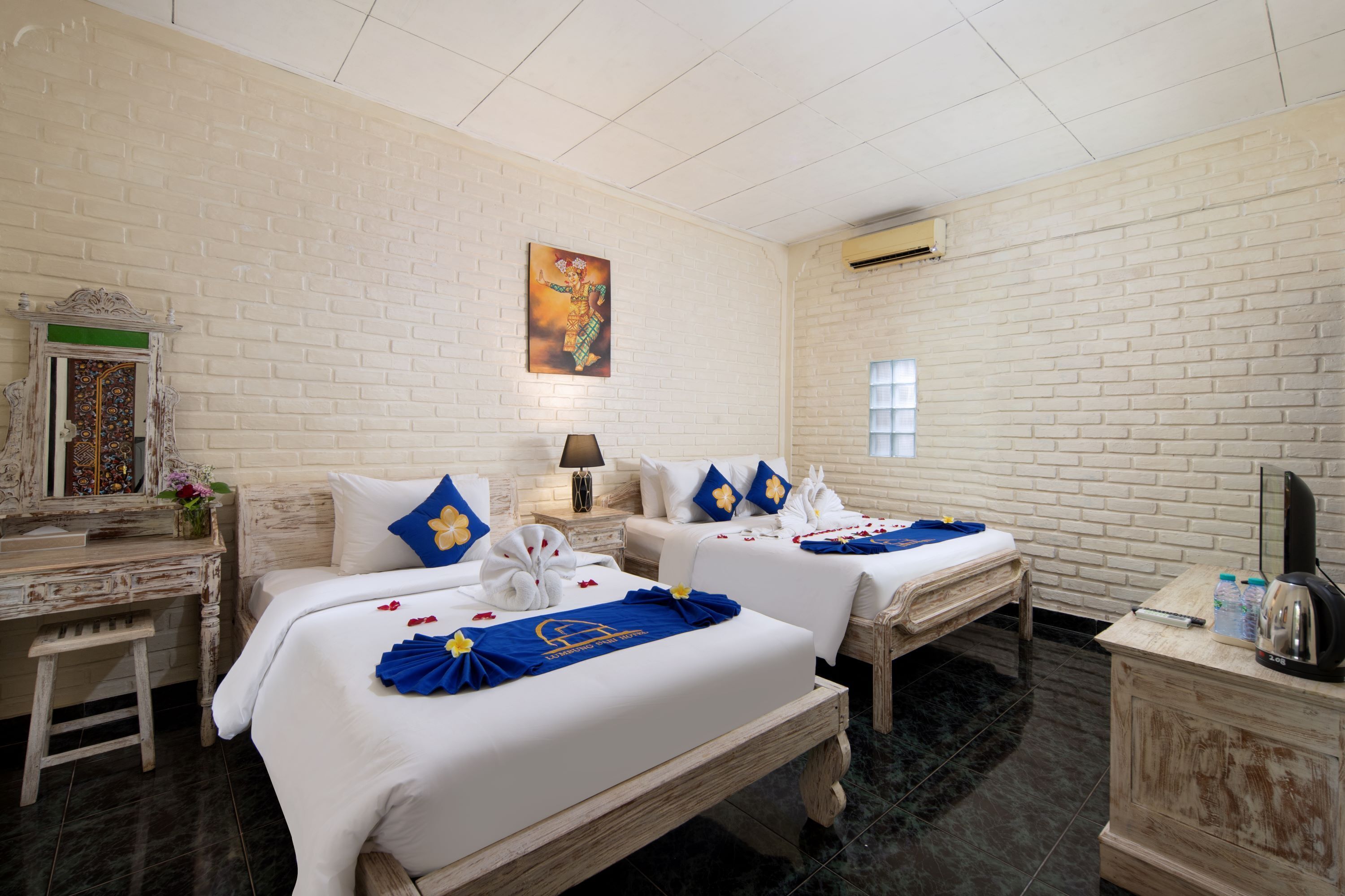 A hotel room with two beds, a desk, a vanity, and a painting on the wall.