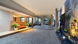A covered outdoor area with a paved walkway, benches, potted plants, and a wall with decorative artwork. - Hotel Lumbung Sari Legian (Legian)